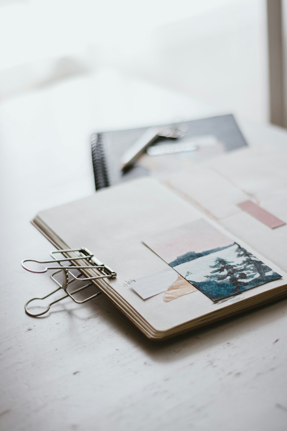 Cuaderno con pintura de paisaje invernal sobre escritorio de madera.