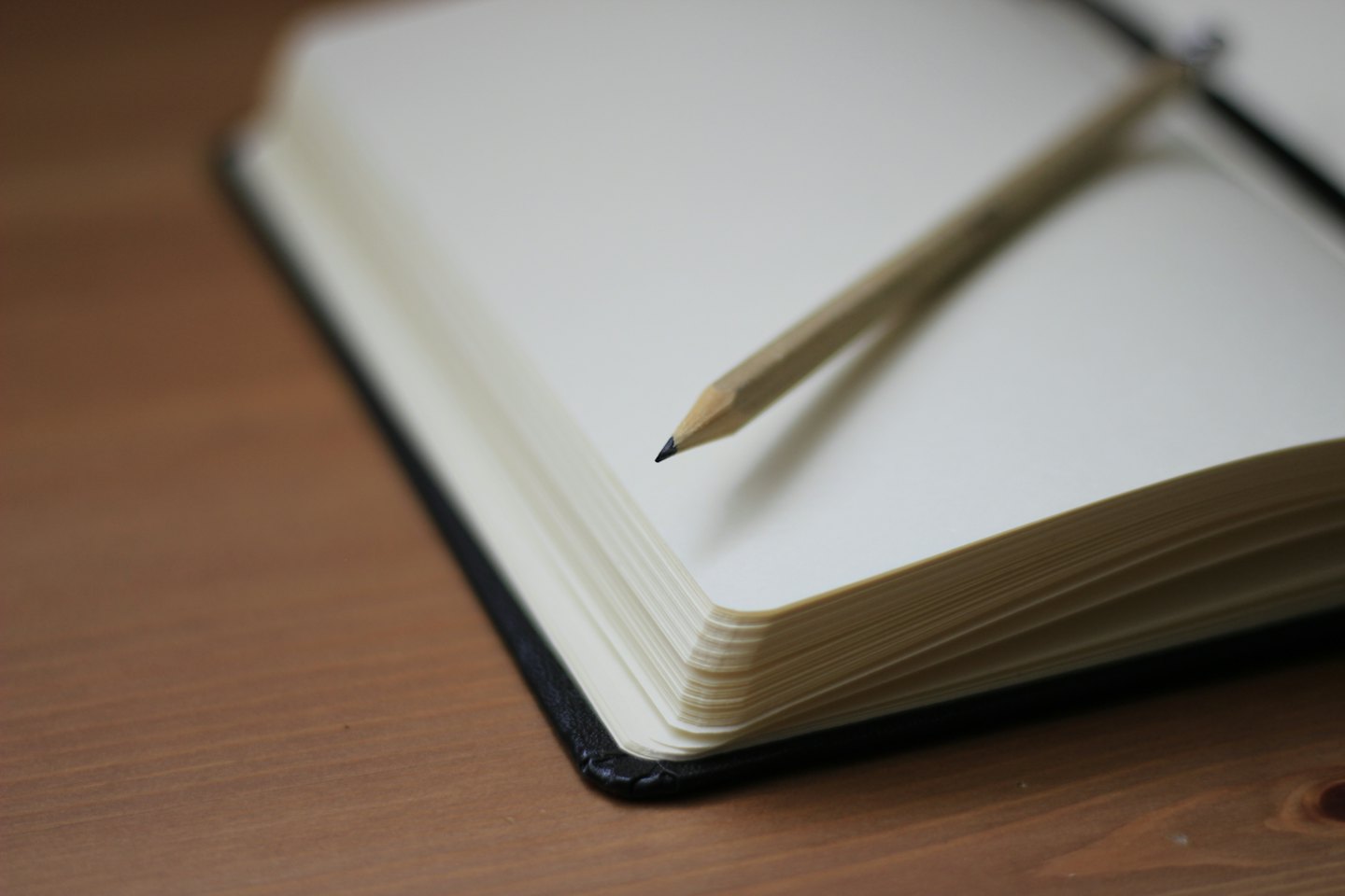 Un lápiz descansa sobre un cuaderno abierto y en blanco en un escritorio de madera.