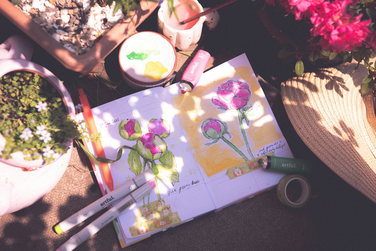 Materiales de arte y diario con bocetos de peonías a la luz del sol.